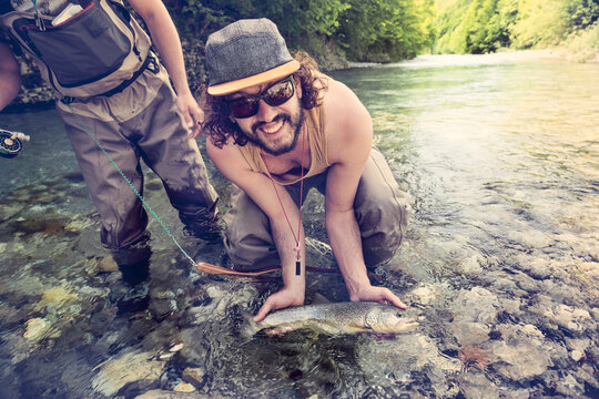 Slovenia, two men fly fishing in Soca river catching a fish