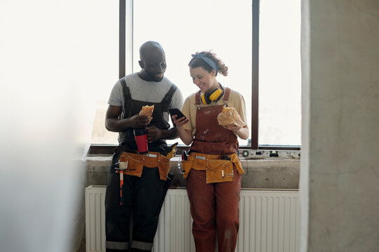 Smiling construction workers taking lunch break and using smart phone at site