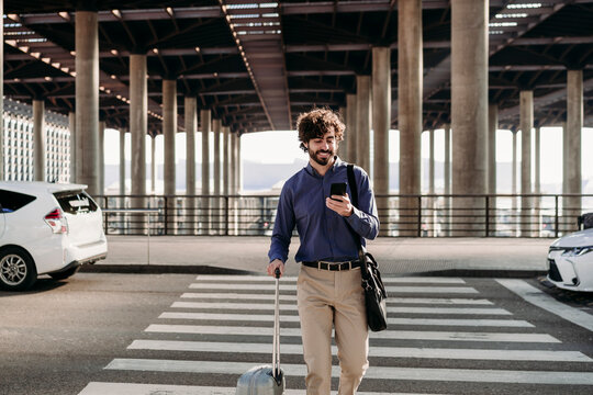 Happy businessman with luggage using smart phone on street