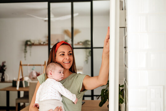 Happy mother carrying baby daughter and touching radiator at home