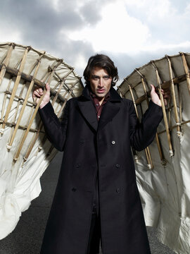 Man holding large constructed angel wings under cloudy sky