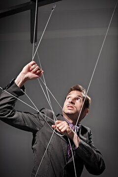 Businessman in suit struggling with puppet string indoors