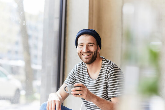 Portrait of smiling young man holding coffee cup at the window