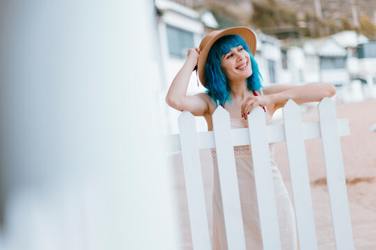 Smiling woman with blue hair leaning on a white fence outdoors