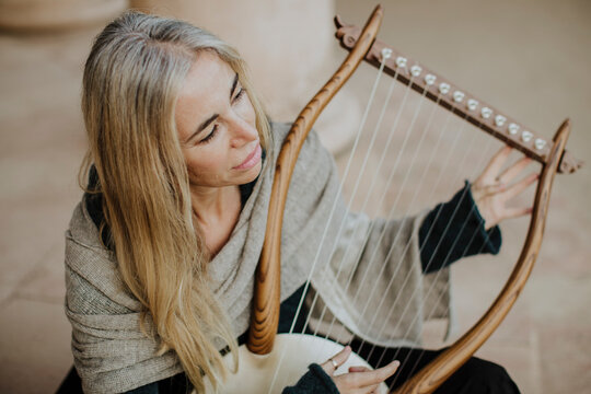 Focused artist playing a wooden harp in peaceful concentration