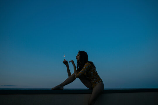 Silhouette sitting at dusk against a blue sky holding a sparkler