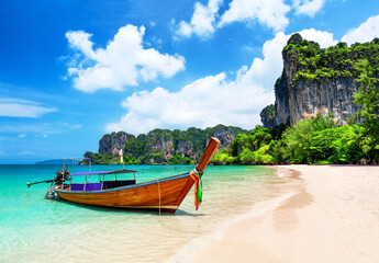 Obraz premium Traditional longtail boat resting on the white sand of Railay Beach near Ao Nang, Thailand. Tropical scenery with turquoise water and dramatic limestone cliffs.