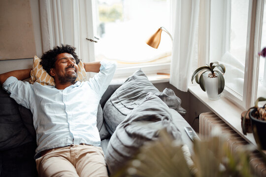 Smiling man with eyes closed resting on sofa at home