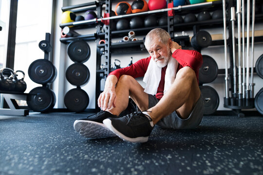 Exhausted senior man sitting on the floor after working out in gym
