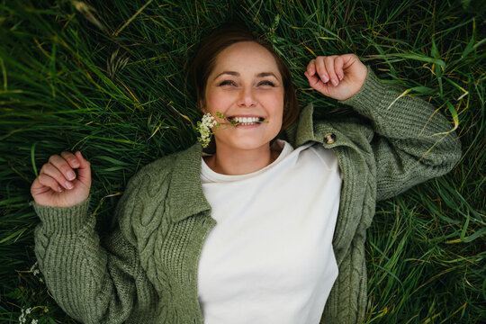 Lying in lush green grass with a flower in mouth for self care