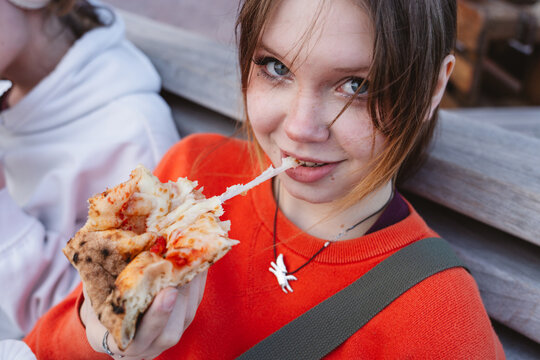 Eating a slice of pizza with stretching cheese outdoors