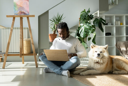 Customer service representative working on laptop by dog on floor at home
