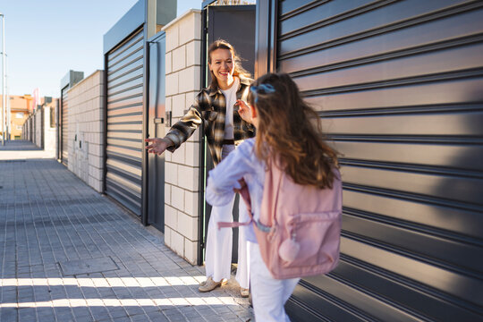 Happy mother welcoming daughter home from school outdoors
