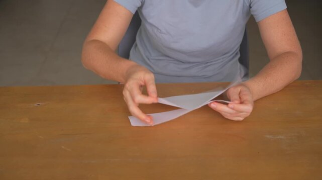 Woman tearing a sheet of paper into many pieces at a table, high quality audio recording. Sharp ripping sounds and expressive action. Emotion, stress relief and everyday lifestyle concept.