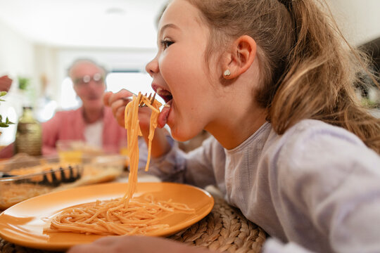 Child eating spaghetti with family at home