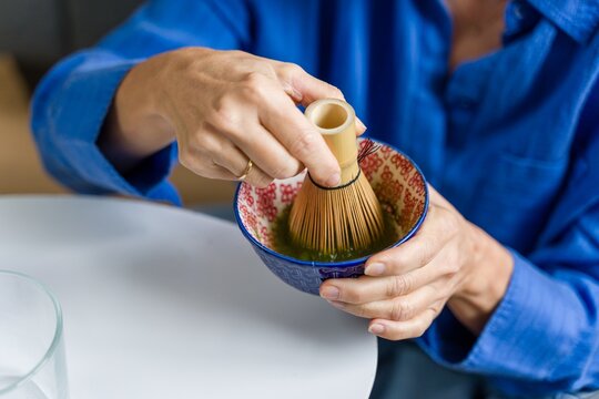 Woman preparing matcha green tea with a bamboo whisk at home