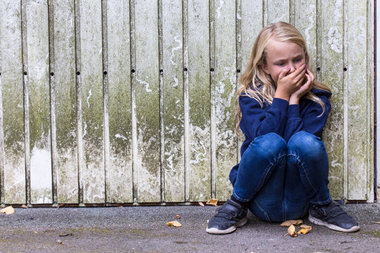 Frightened girl crouching in front of wooden wall