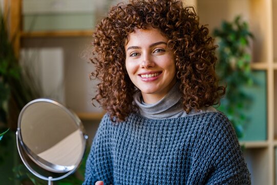 Smiling curly haired woman beside a vanity mirror indoors
