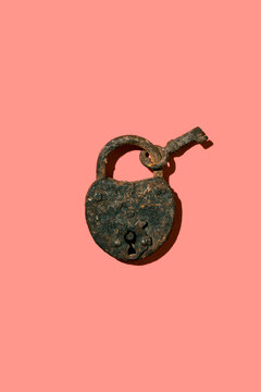 Antique rusted heart shape padlock with key on pink background