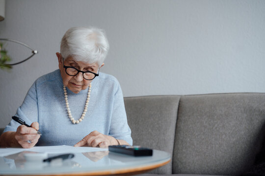 Senior woman doing paperwork sitting on sofa at home