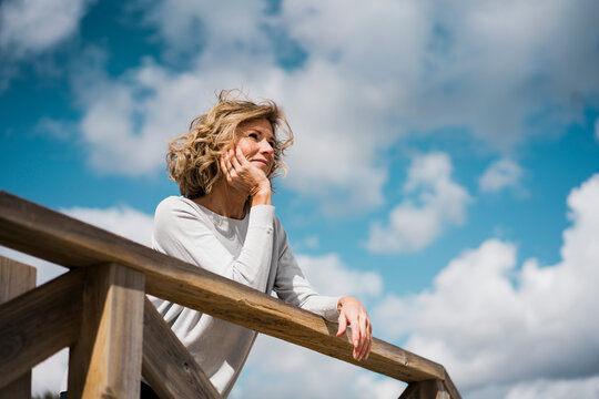 Smiling blond woman leaning on railing under cloudy sky