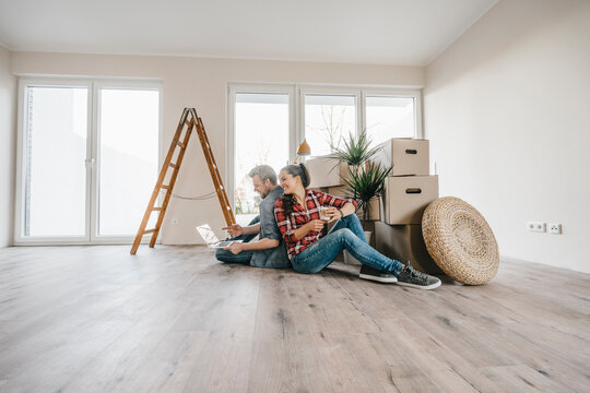 Couple sitting on floor of their new home among moving boxes