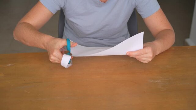 Woman cutting a sheet of paper into strips with scissors at a table, high quality audio recording. Sharp cutting and snipping sounds. Craft process, precision and everyday lifestyle concept.