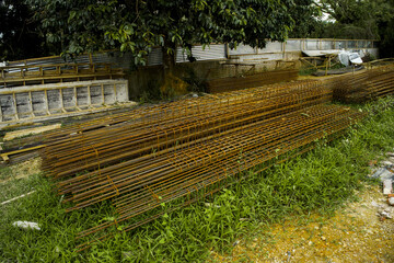 Obraz premium Stack of rusty steel rebar cages on grassy ground at a construction site