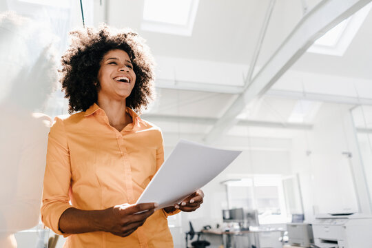 Laughing young woman holding documents in office