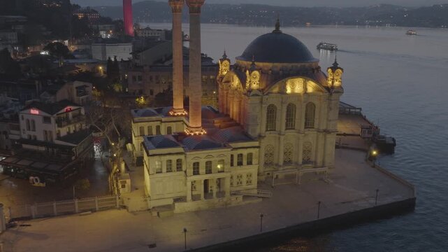 Aerial view of the illuminated Ortak&ouml;y Mosque on the shores of the Bosphorus in Istanbul, Turkey, with the iconic Bosphorus Bridge in the background.