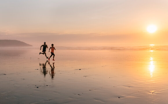 Athletes couple running on the beach at sunset