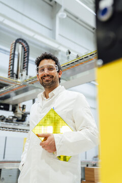 Engineer in a factory wearing safety glasses and holding a new product