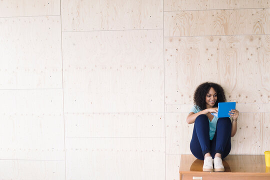 Young woman sitting under white board using laptop