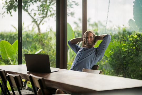 Handsome man with laptop sitting at modern wooden table in contemporary design house