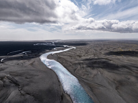 Glacial river flows through dark volcanic plains of Skei�ar�rsandur