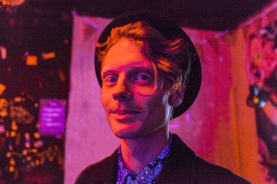 Young man wearing hat during psychedelic party, effects of light machine on a wall