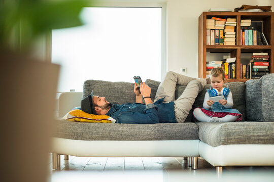 Father and daughter with digital tablet and smartphone on sofa