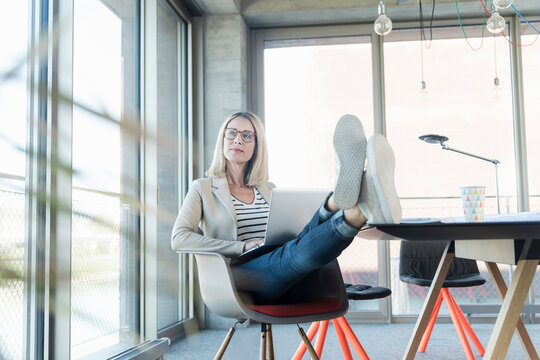 Relaxed businesswoman using laptop in office with feet up