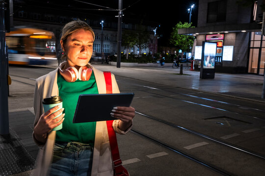 Smiling commuter with tablet and coffee in city at night