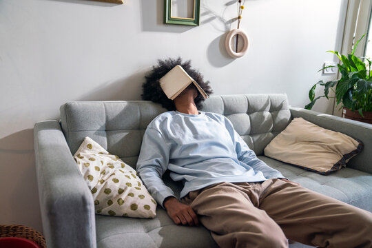 Man with book on face sleeping on sofa at home