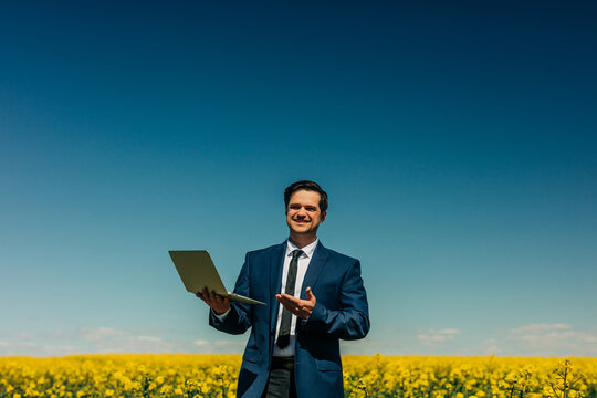 Smiling businessman with laptop in a yellow rapeseed field