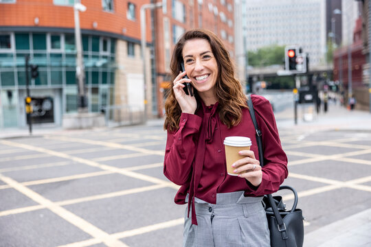 Smiling businesswoman talking through smart phone standing on city street
