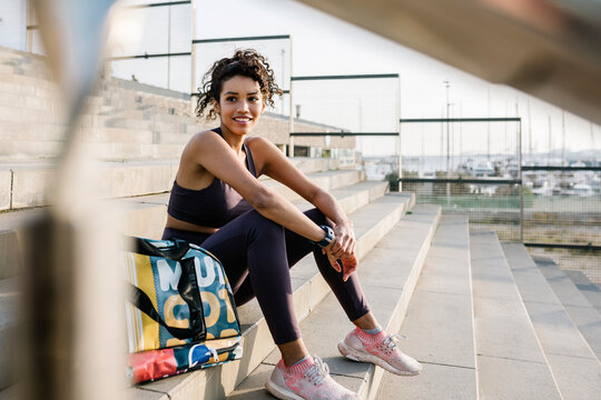 Smiling sportsperson day dreaming while sitting by bag on staircase