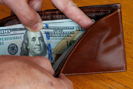 Hand taking a 100 dollar bill banknote from wallet, cost of living, wages, or inflation concept.