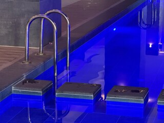 Blue ambient lighting illuminating indoor swimming pool ladder and tiled lanes at night background © dvoevnore