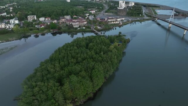 High angle drone shot of Anaklia coastal resort in Georgia, showing the famous pedestrian bridge, green river island, and scenic sea delta landscape.