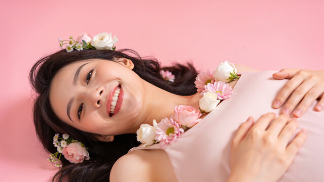 Smiling woman lying on pink background with flowers on her hair. concept of happiness