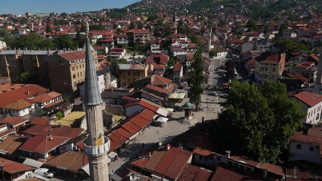 Cinematic Drone Hover of Bascarsija Mosque Minaret, Aerial View of Sebilj Fountain and Pedestrians in Historic Market Square of Old Town Sarajevo Bosnia, 4K