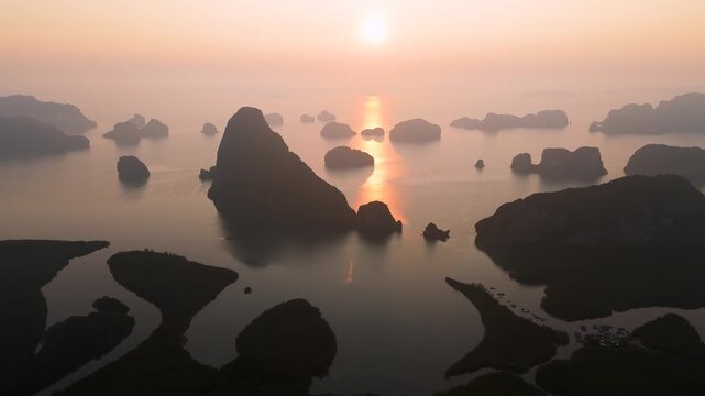 Aerial view majestic limestone formations rise above emerald waters fringed by winding mangroves, with a bustling coastal village visible at orange sunrise bright orange clouds.