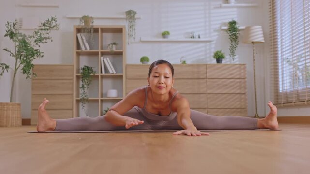 Girl split yoga stretch exercise home floor indoor flexibility child practicing calm fitness pose on wooden mat bright living room interior plant window blind cabinet wellness routine